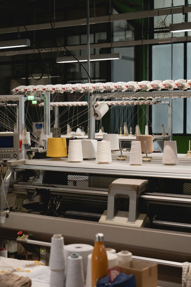 Machine room with electronic knitting machines and coloured yarn cones